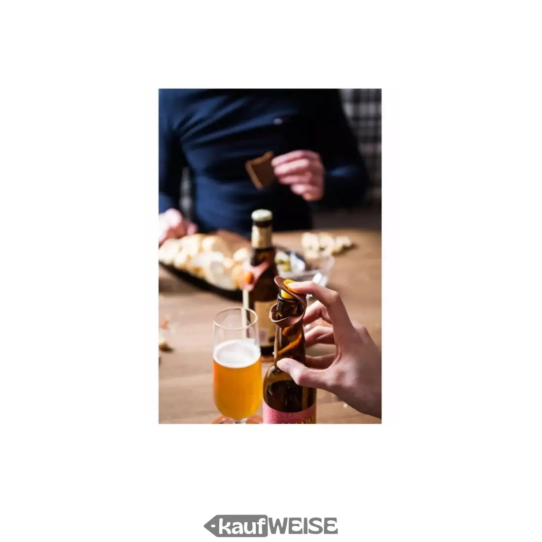 Person am Tisch hält Bierflasche mit Flaschenmarker aus Kunstleder neben einem Glas Bier